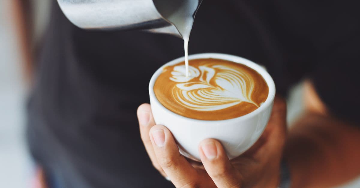 Barista pouring milk to create latte art in a coffee cup